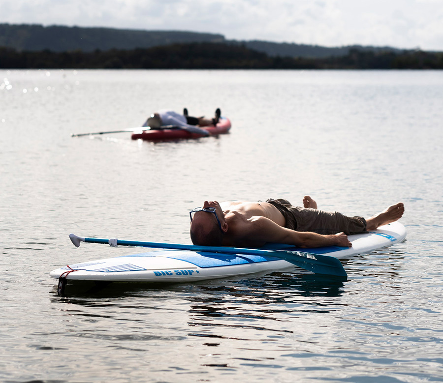 Homme allongé sur un paddle au milieu du lac